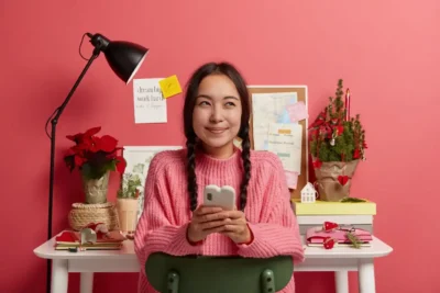 Imagem de uma jovem sorridente segurando um celular frente a uma mesa com decorações, representando a ideia do Instagram como microblogging.