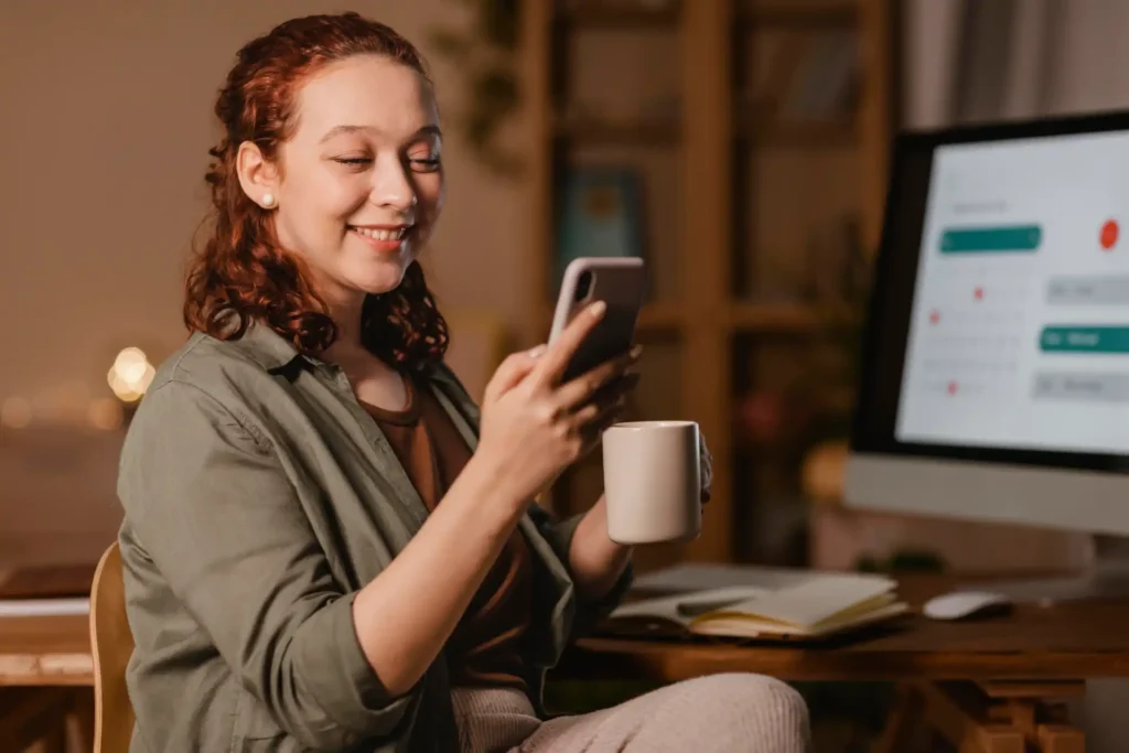 Mulher utilizando smartphone enquanto toma café, em ambiente de trabalho, ideal para validar páginas AMP no Search Console.