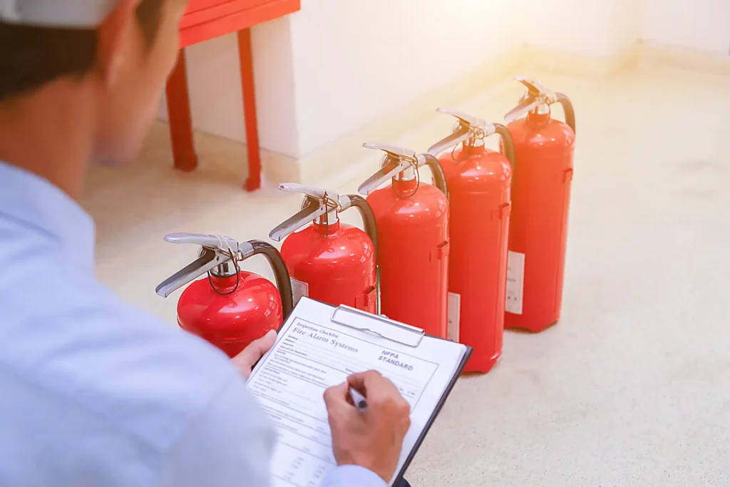 Homem conferindo documento ao lado de extintores de incêndio alinhados, ilustrando passos importantes para contratar uma empresa confiável de manutenção de extintores.