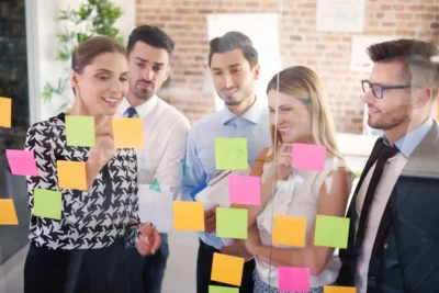 Equipes de trabalho discutindo estratégia, com post-its coloridos, em ambiente de escritório moderno, representando dicas para montar uma equipe de alta performance.
